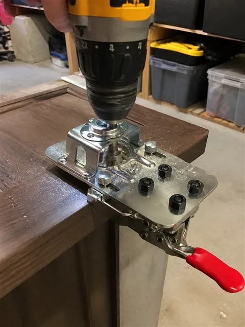 Hinge jig guiding a drill on a walnut cabinet door
