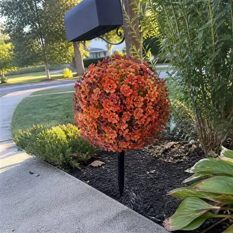 Artificial flower topiary staked in a garden bed near a walkway