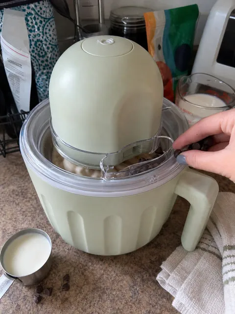 Chocolate chips being added to the ice cream maker on a home kitchen counter