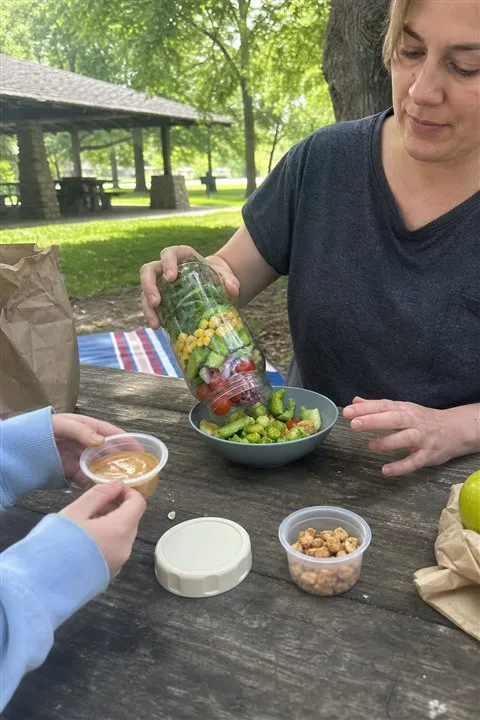 Salad jar being poured into a bowl at a park picnic table