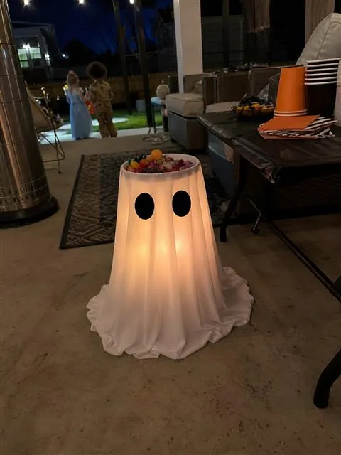 Glowing ghost candy bowl beside a casual nighttime patio snack table