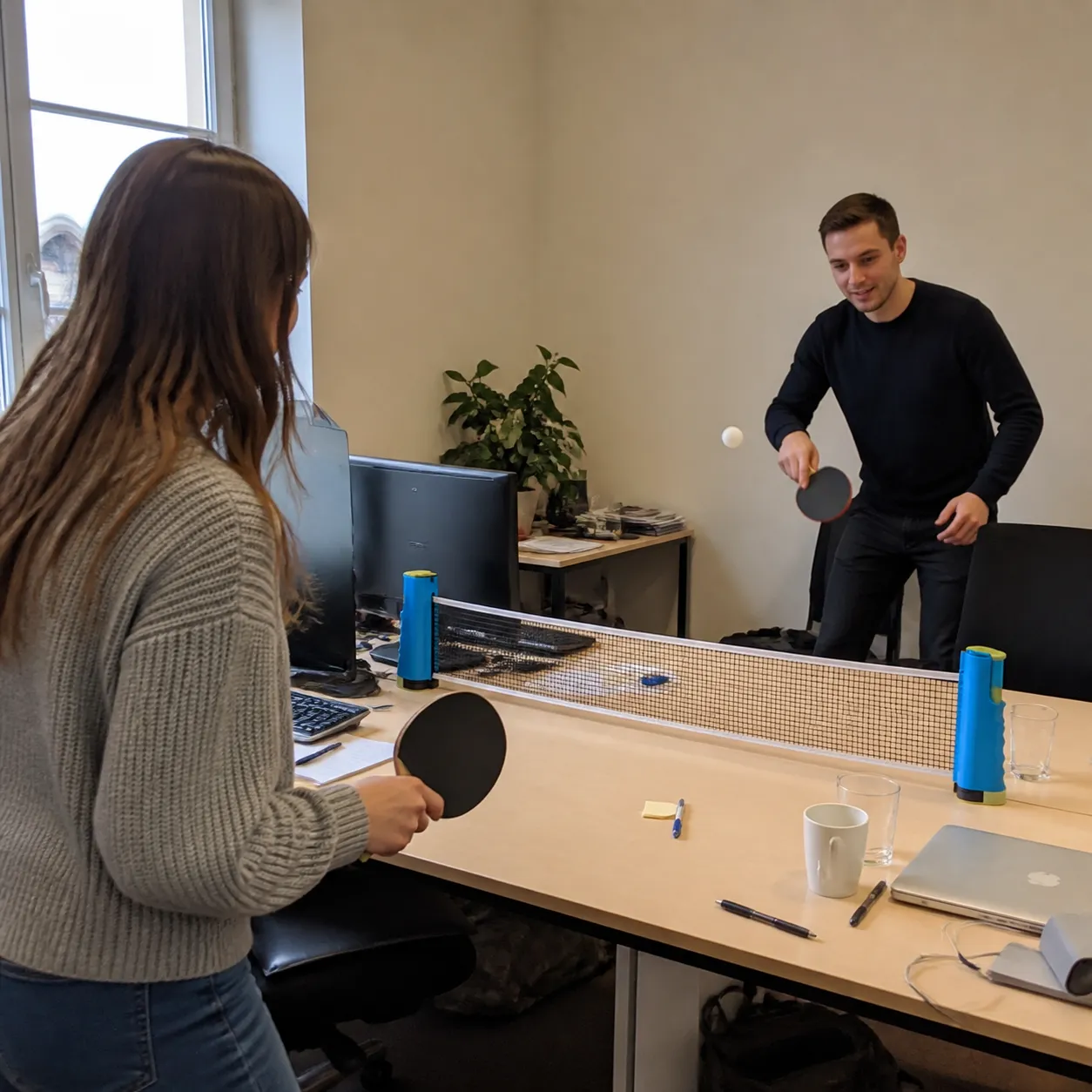Coworkers playing table tennis across an office desk