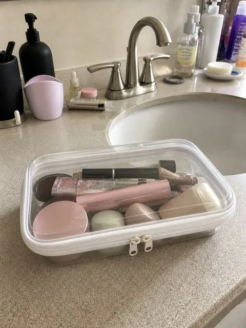 Closed clear white-trim organizer holding makeup beside a bathroom sink