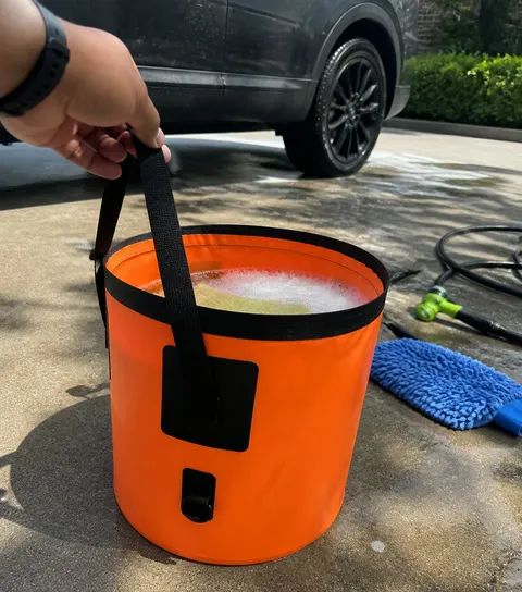 Orange collapsible bucket with soapy water beside an SUV