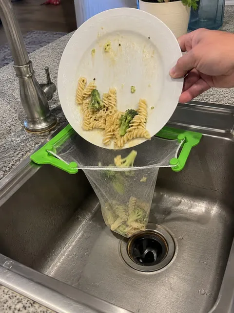 Pasta being tipped into a mesh strainer bag over a kitchen sink
