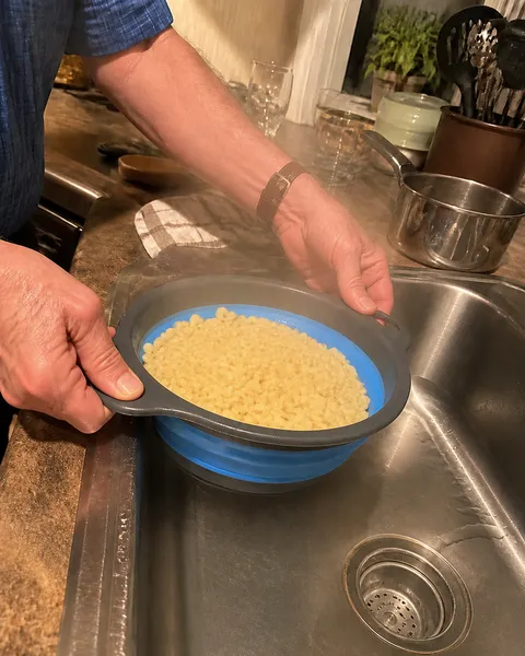 Older cook draining pasta in the medium blue colander