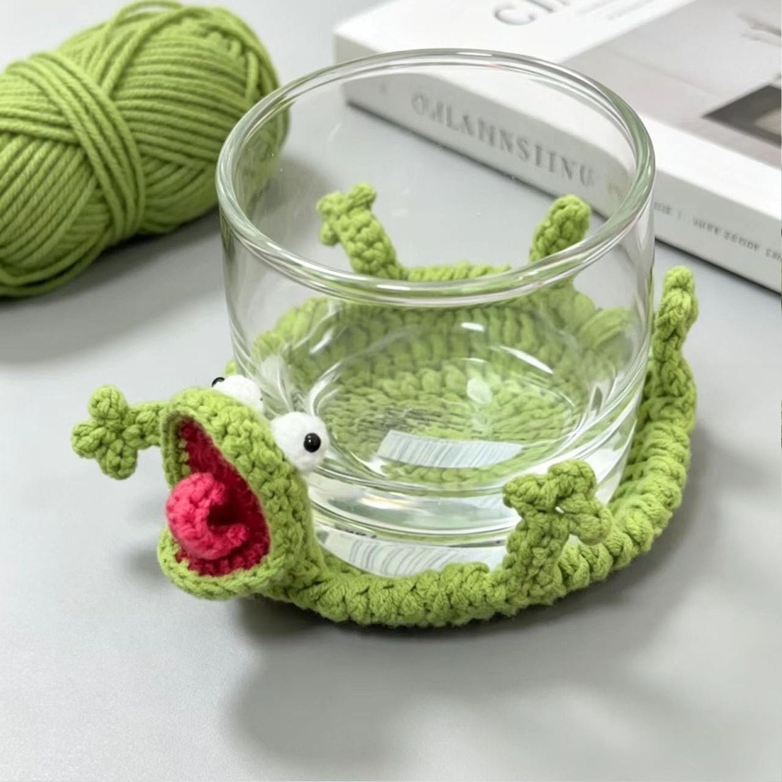 Clear glass sitting inside a green crochet lizard coaster with a funny popping tongue
