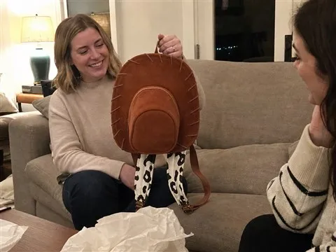Adult holding a brown cowboy hat backpack during a living room gift moment