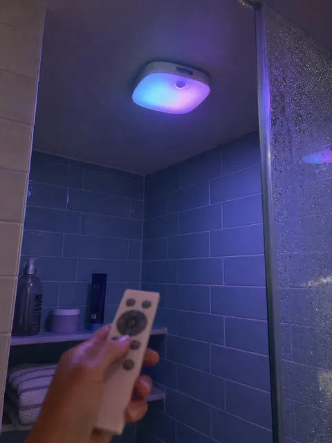 Remote changing the shower light color in a blue-tile bathroom