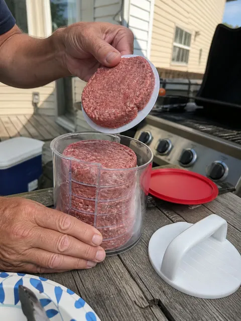 Backyard cook lifting a formed hamburger patty beside the grill