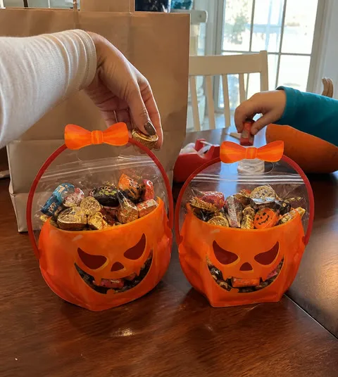 Parent and child filling two orange pumpkin bags at a kitchen table