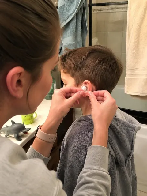 Parent applying a clear ear cover before bath time
