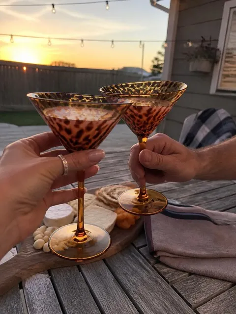 Two people toasting with amber tortoiseshell martini glasses on a backyard patio
