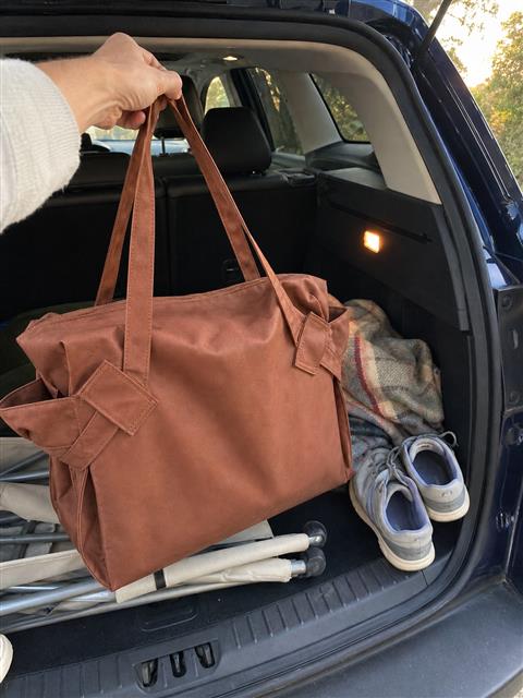 Brown tote being lifted from an SUV trunk Brown tote being lifted from an SUV trunk