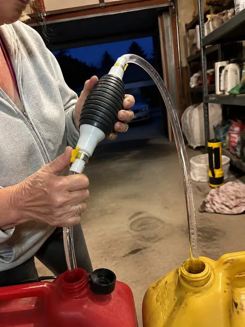 Hands using a manual siphon pump in a home garage
