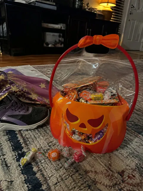 Filled orange pumpkin bag beside a child's costume and shoes after trick-or-treating