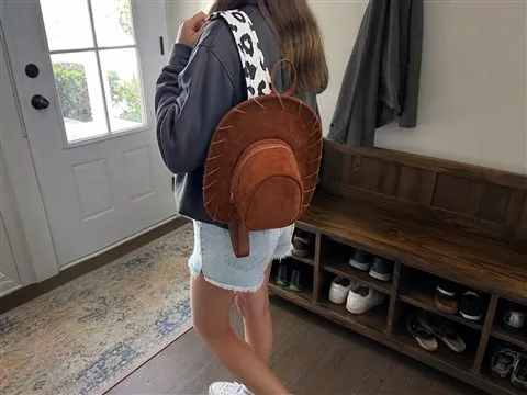 Person adjusting a cow-print backpack strap in a bright entryway