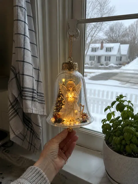Angel light-up bell ornament hanging in a snowy kitchen window