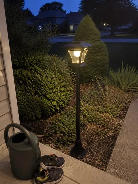 Solar courtyard lamp glowing beside a porch at blue hour