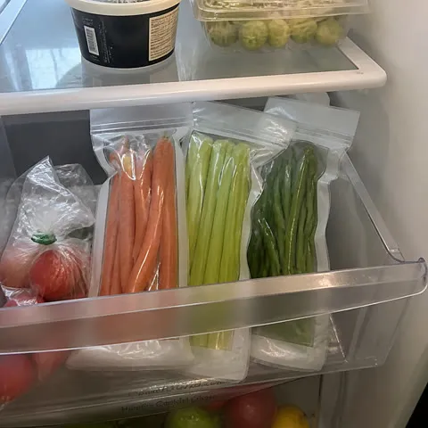 Organized refrigerator drawer with carrots, celery, and green vegetables in clear bags