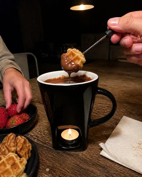 Black chocolate fondue mug with waffle bites and strawberries