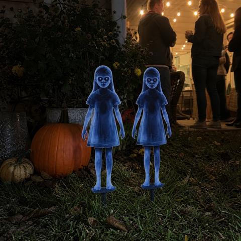 Two ghost-girl stakes near pumpkins during a backyard Halloween gathering