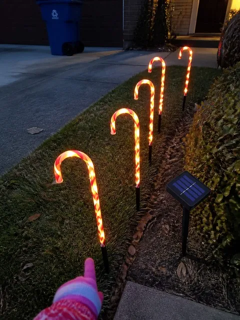 Five candy cane lights glowing along a front lawn