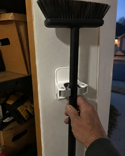 Hand removing a push-broom handle from a wall gripper in a garage