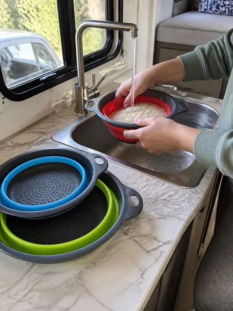 Rice being rinsed in the small red colander inside an RV kitchenette