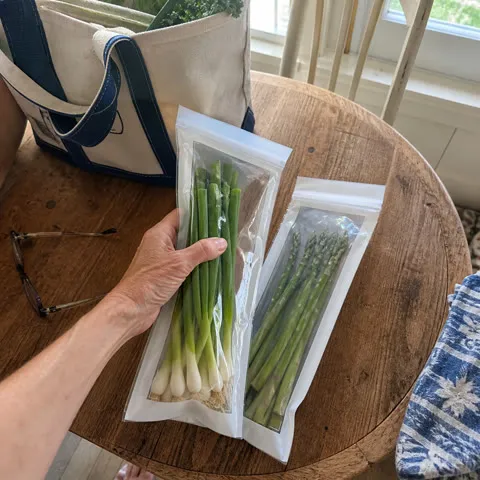 Scallions and asparagus packed in long clear storage bags on a wooden table
