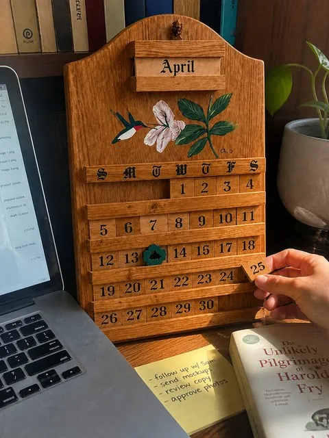 A wooden calendar on a lived-in home office shelf