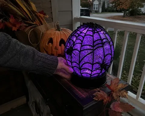 Spider glitter globe on a covered porch beside a pumpkin