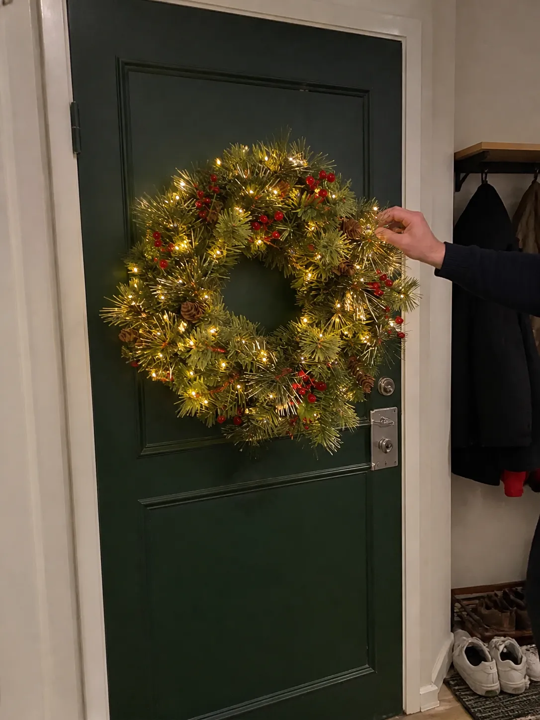 Lit wreath being adjusted on a green entry door