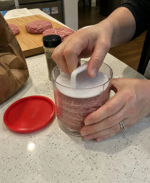 Home cook pressing a batch of hamburger patties in a clear manual patty press