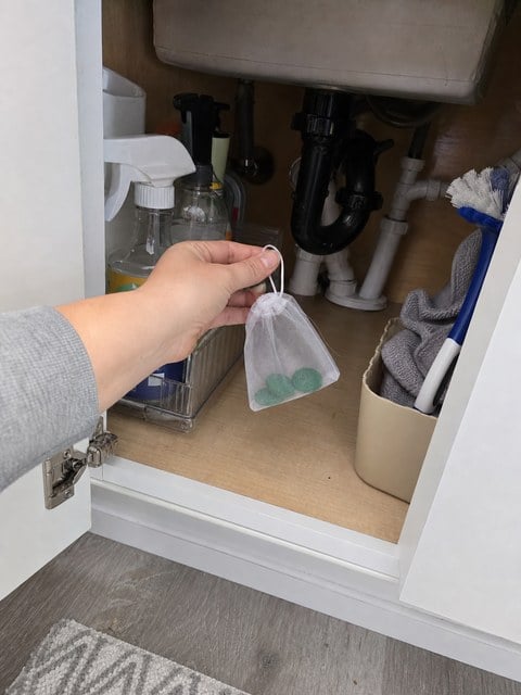 Mesh pouch being placed inside an under-sink cabinet