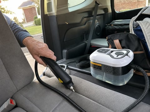 Customer using the white steam cleaner on car seat seams