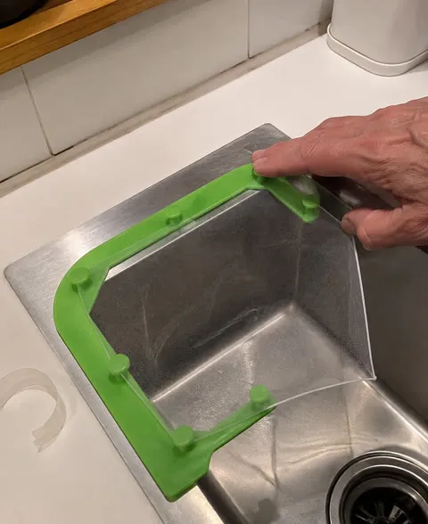 Older hand pressing a green sink strainer holder into place