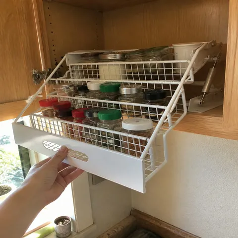 White pull-down rack filled with baking spices in an oak cabinet