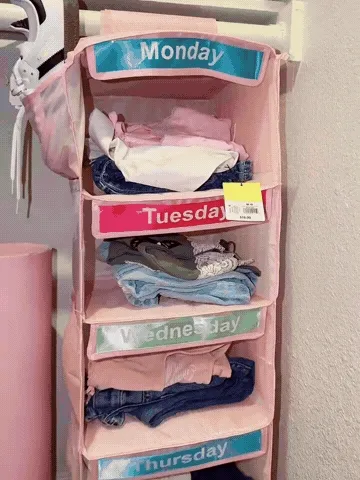 Pink weekday hanging organizer being filled with folded outfits