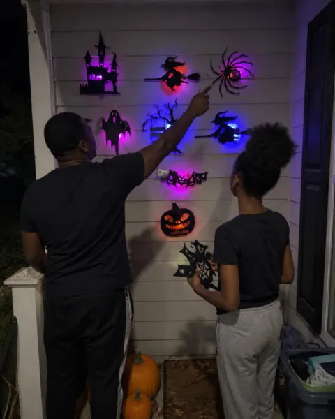 Family arranging glowing Halloween decorations on a covered porch