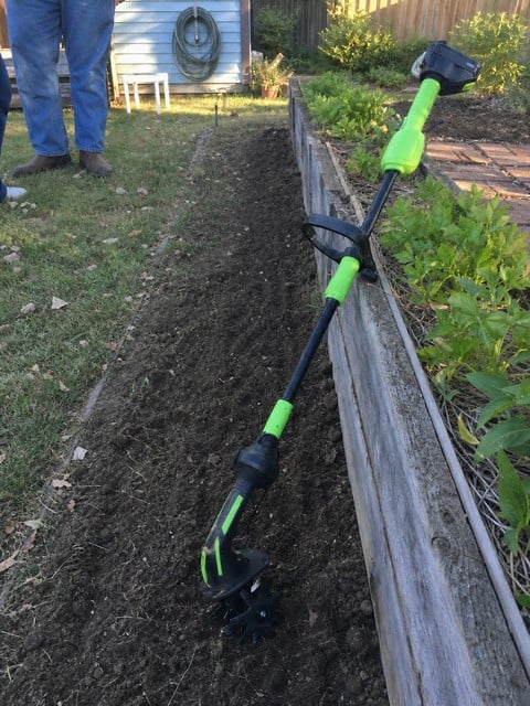 Cordless tiller resting beside a freshly worked narrow garden row