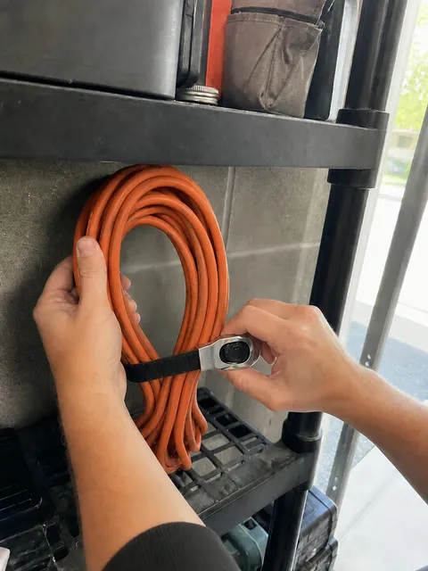 Hands organizing cords and a hose in a garage