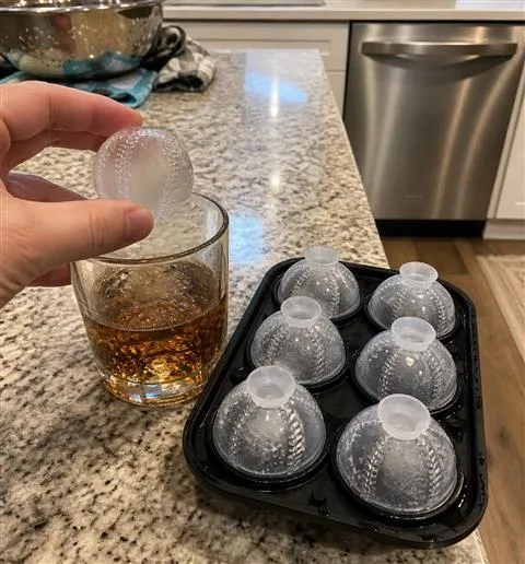 Baseball ice sphere being added to a home drink