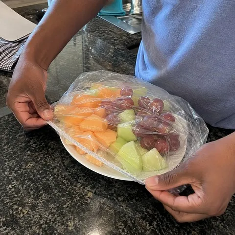 Hands fitting a cover over a fruit plate