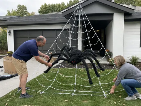 Couple setting up a large spider web decoration in front of a garage
