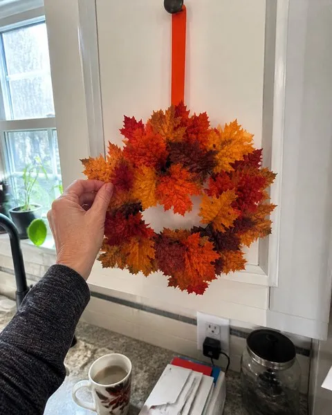 Fall maple leaf wreath being fluffed on a white kitchen cabinet