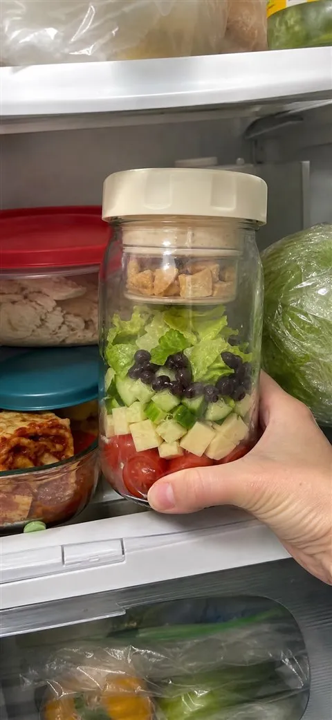 Prepared layered salad jar being placed on a refrigerator shelf
