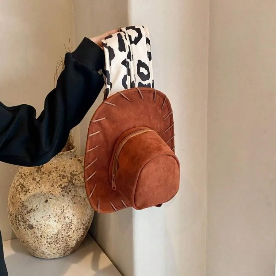 Close view of the brown cowboy hat backpack and cow-print straps