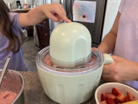 Child pressing the one-touch button while a parent steadies the ice cream maker