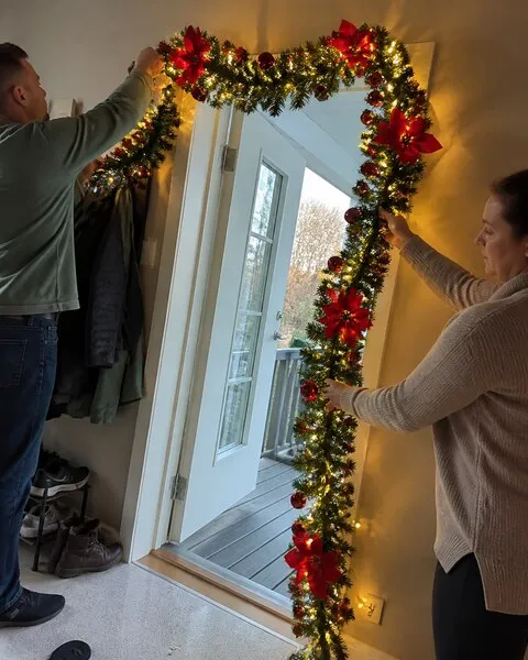 Two adults placing Christmas garland around a home entryway